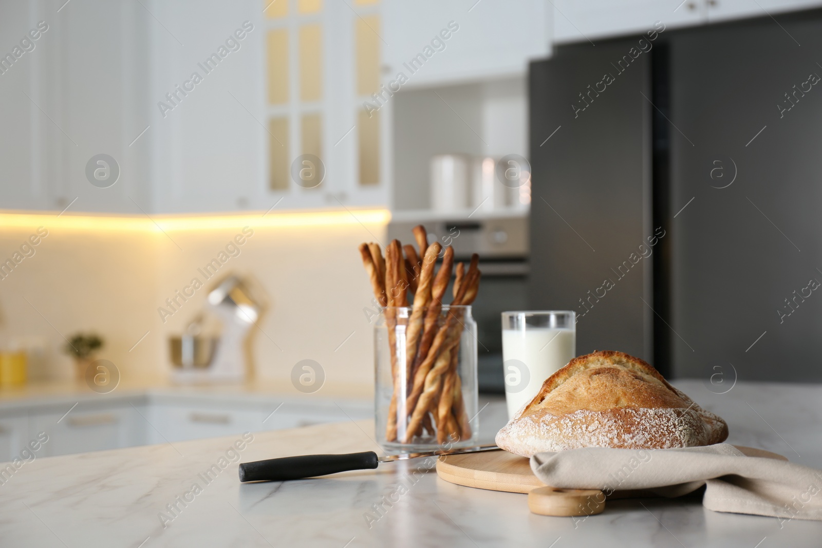 Photo of Loaf of bread, glass with milk and grissini on white table in kitchen. Space for text