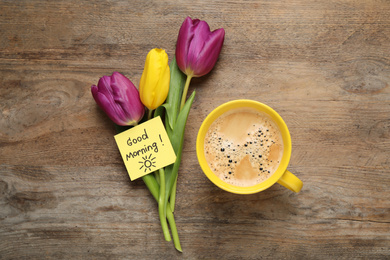 Photo of Delicious coffee, flowers and card with GOOD MORNING wish on wooden table, flat lay