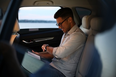 Handsome man using tablet on backseat of modern car