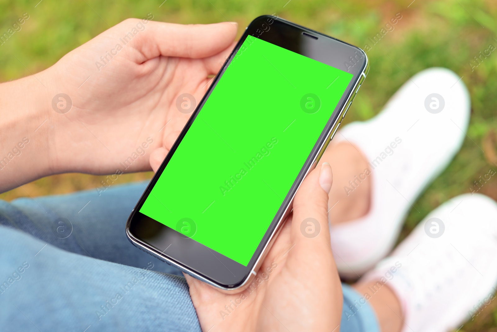 Image of Woman holding smartphone with green screen outdoors, closeup. Gadget display with chroma key. Mockup for design