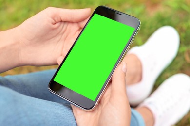 Woman holding smartphone with green screen outdoors, closeup. Gadget display with chroma key. Mockup for design