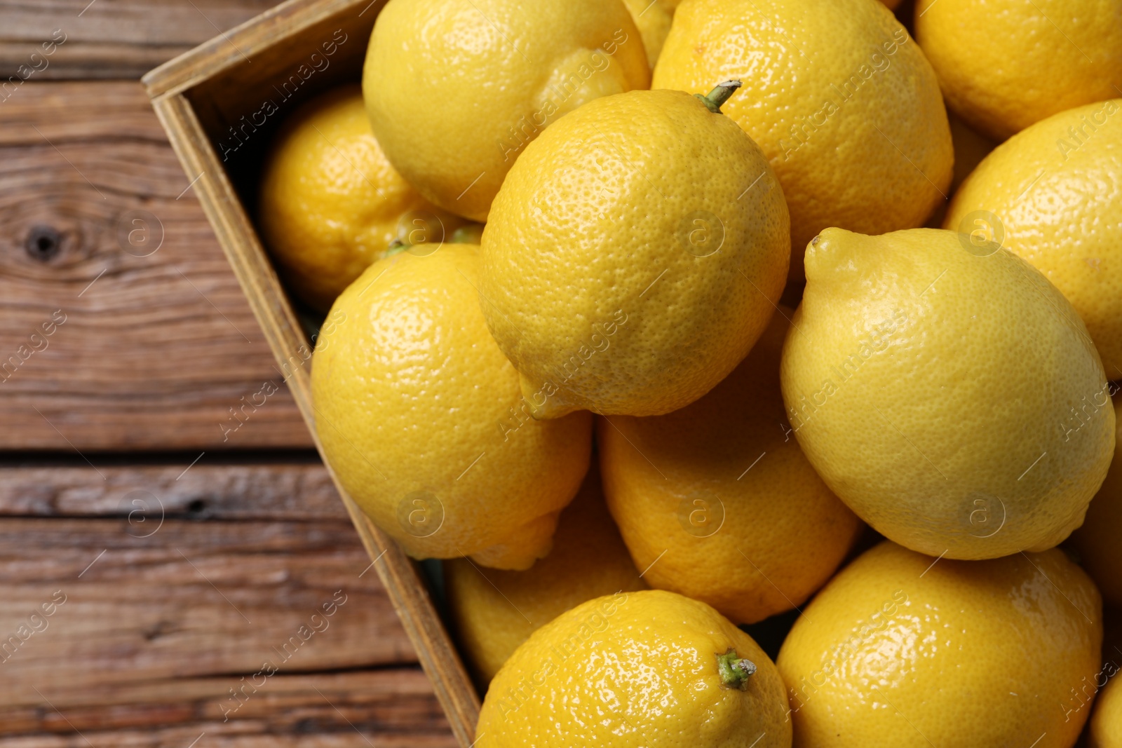 Photo of Fresh lemons in crate on wooden table, top view