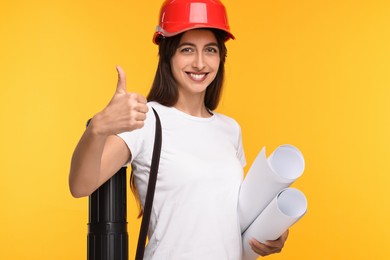 Photo of Architect in hard hat with drafts and tube showing thumbs up on yellow background
