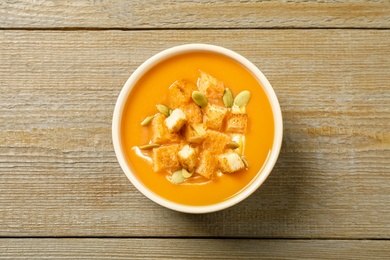 Photo of Tasty creamy pumpkin soup with croutons and seeds in bowl on wooden table, top view