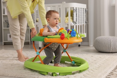 Mother and her little son at home. Cute baby making first steps with toy walker