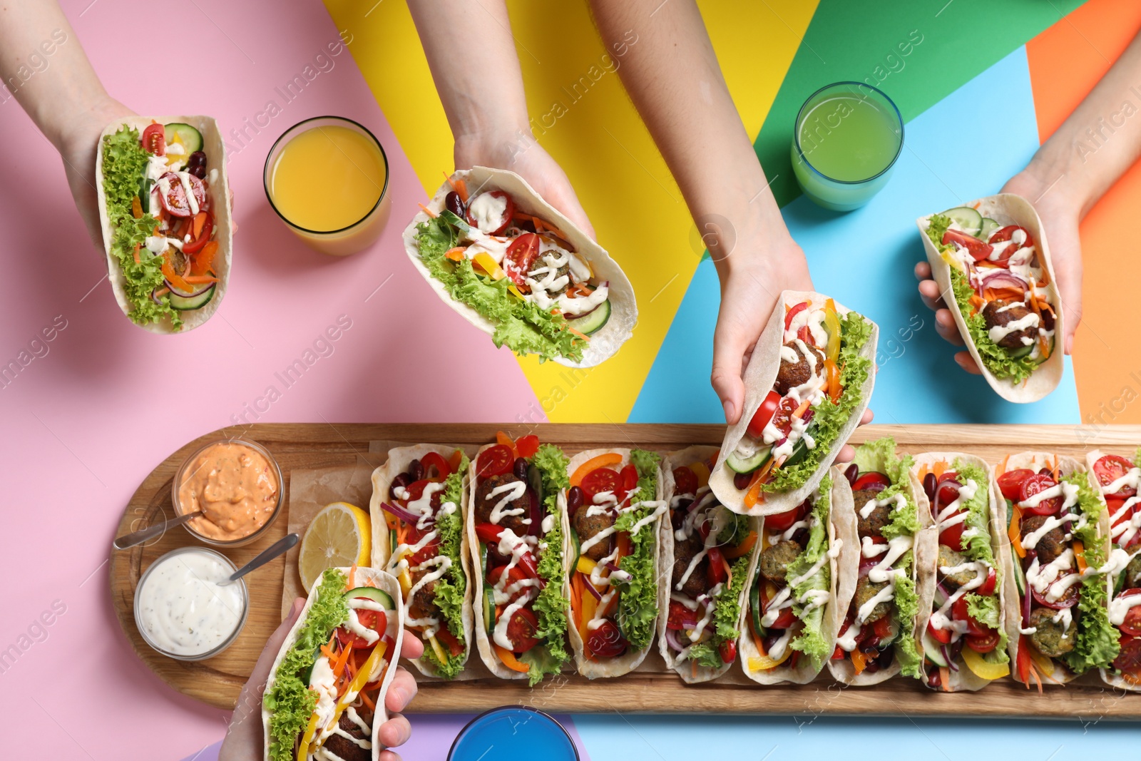 Photo of Friends holding delicious tacos on color background, top view