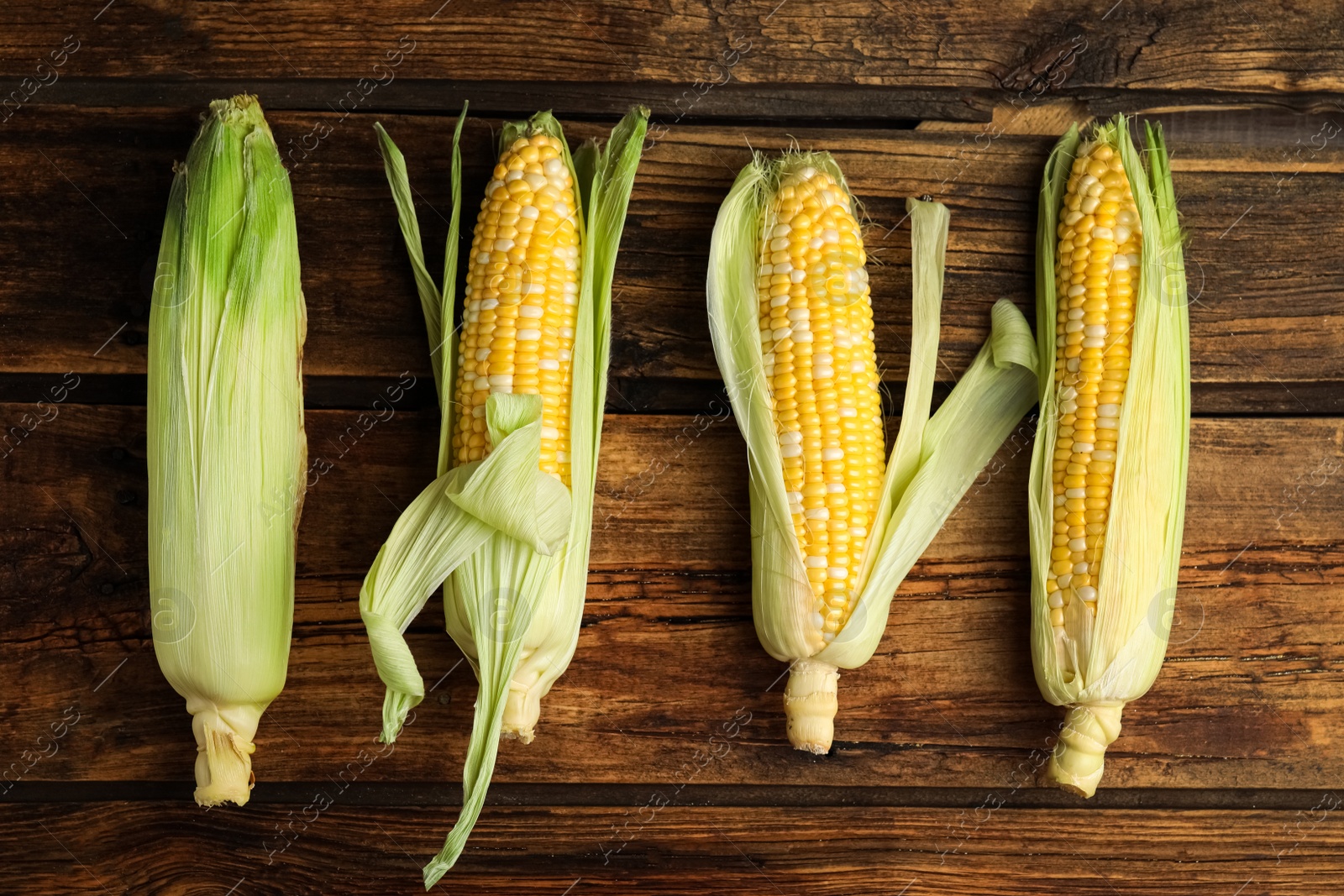 Photo of Tasty sweet corn cobs on wooden table, flat lay