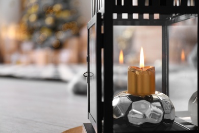 Burning candle in lantern against blurred background, space for text. Stylish interior element