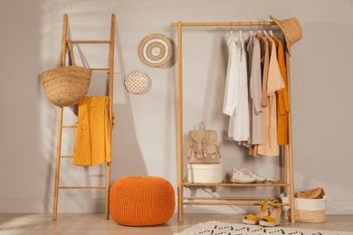 Photo of Modern dressing room interior with stylish clothes, shoes and orange pouf