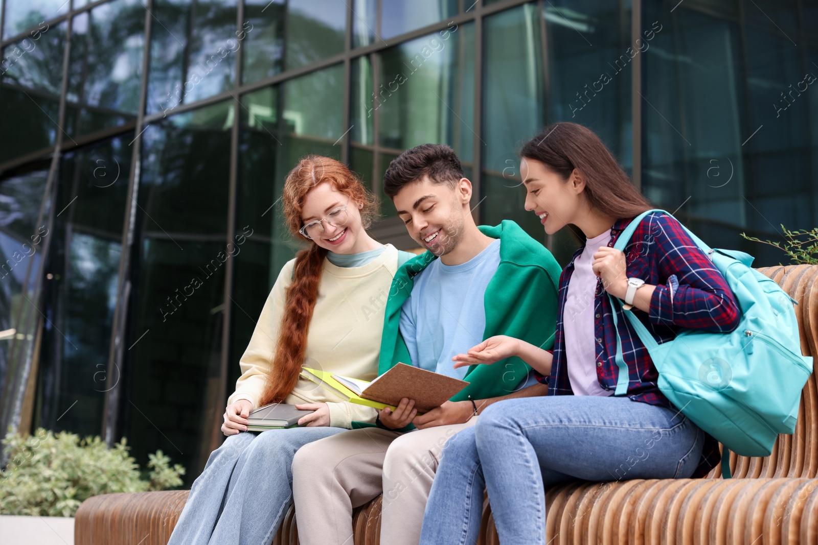 Photo of Happy young students studying with notebooks on bench outdoors