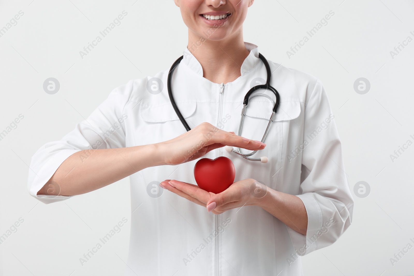 Photo of Doctor with stethoscope and red heart on white background, closeup. Cardiology concept