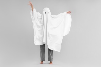 Photo of Woman in white ghost costume on light grey background. Halloween celebration