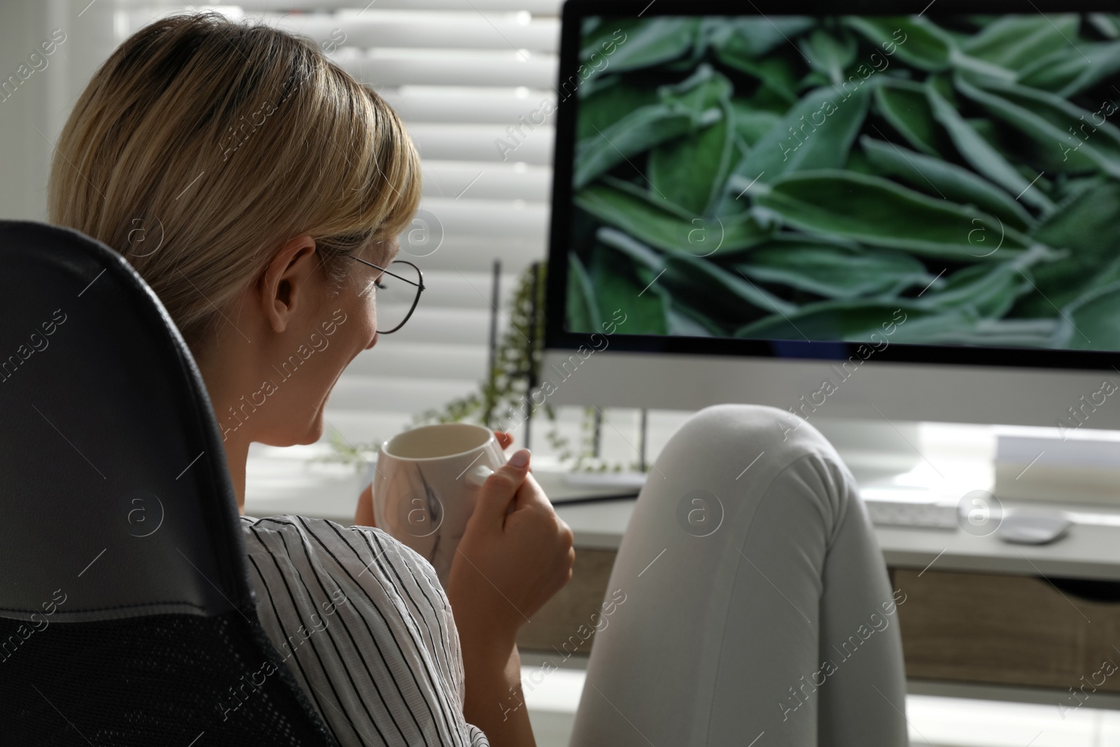 Photo of Woman with cup of drink resting near workplace in room. Interior design