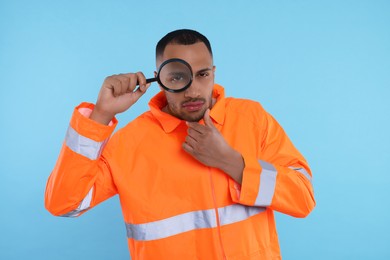 Photo of Curious worker in uniform looking through magnifier glass on light blue background