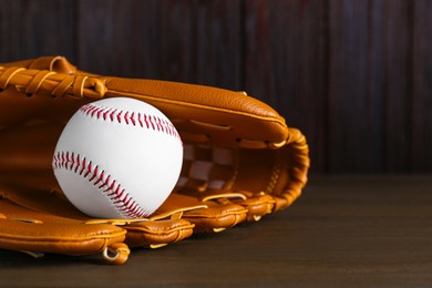 Photo of Leather baseball glove with ball on wooden table. Space for text