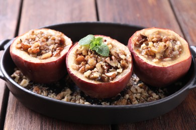 Tasty baked apples with nuts, honey and mint in baking dish on wooden table, closeup