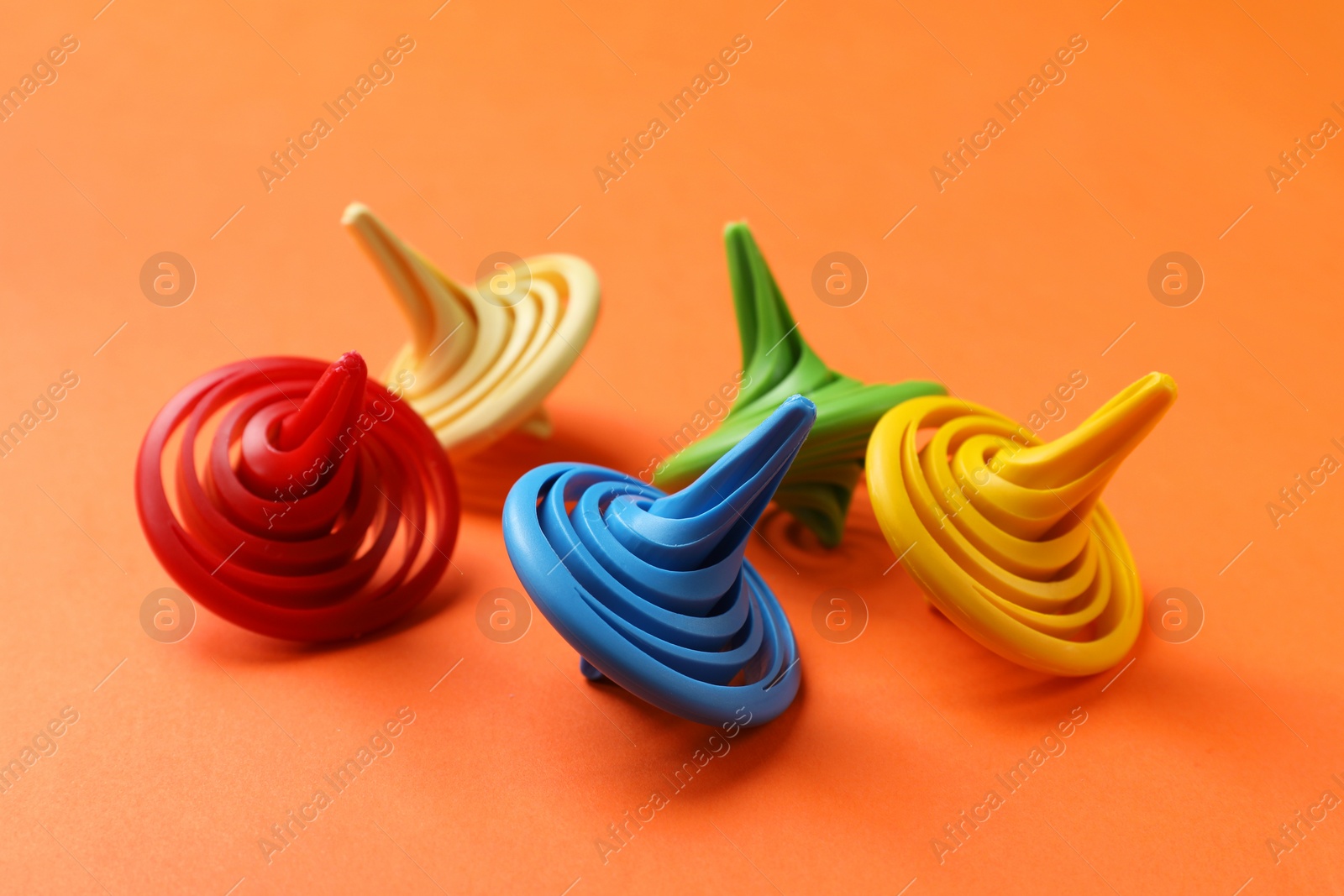 Photo of Many colorful spinning tops on orange background, closeup