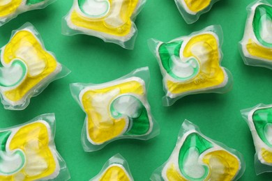 Photo of Many dishwasher detergent pods on green background, flat lay