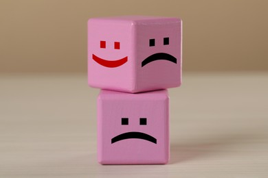 Pink cubes with sad and happy faces on wooden table