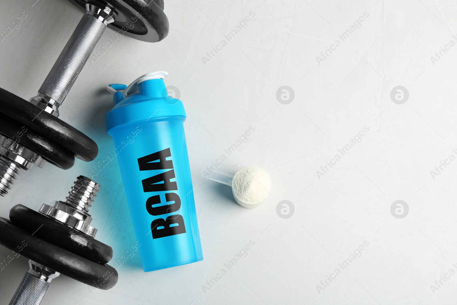 Image of Shaker with abbreviation BCAA (Branched-chain amino acid), dumbbells and powder on white table, flat lay. Space for text