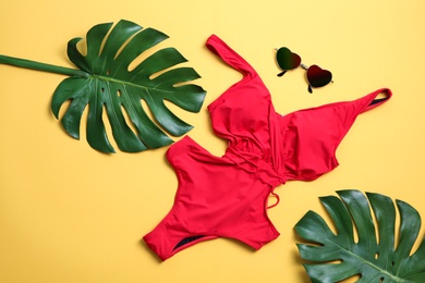 Photo of One-piece swimsuit, sunglasses and tropical leaves on color background