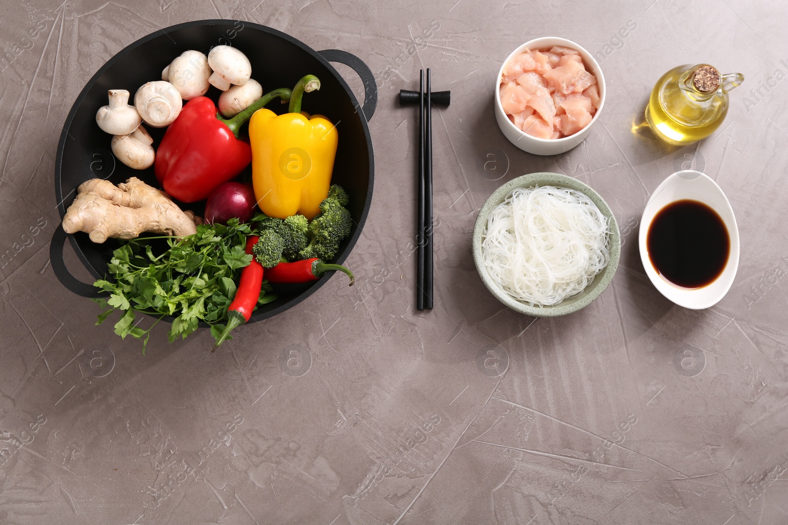 Photo of Wok, chopsticks and different products on grey textured table, flat lay. Space for text