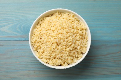 Delicious bulgur in bowl on light blue wooden table, top view