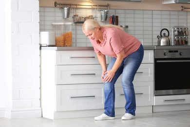 Photo of Senior woman suffering from knee pain in kitchen. Space for text