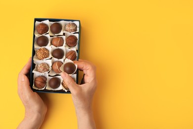 Photo of Woman taking chocolate candy from box on yellow background, top view. Space for text
