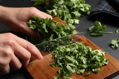 Photo of Woman cutting fresh green cilantro at black table, closeup