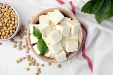 Delicious tofu cheese, basil and soybeans on white tiled table, flat lay