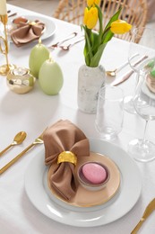 Photo of Festive Easter table setting with painted eggs, burning candles and yellow tulips indoors