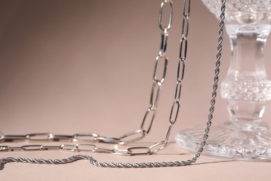 Photo of Different metal chains and glass on light brown background, space for text. Luxury jewelry