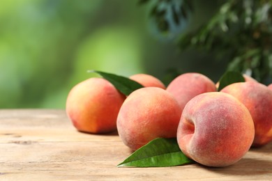Many whole fresh ripe peaches and green leaves on wooden table against blurred background, closeup. Space for text