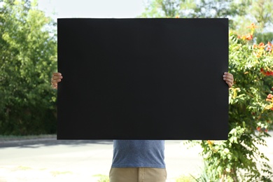 Photo of Man holding black empty poster outdoors. Space for design
