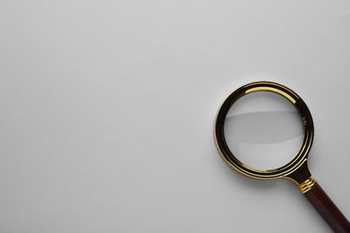 Magnifying glass on light grey background, top view. Space for text
