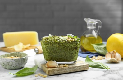 Photo of Delicious pesto sauce and ingredients on white marble table