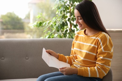 Woman reading letter on sofa at home