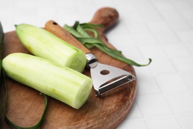 Photo of Fresh cucumbers and peeler on white tiled table, closeup. Space for text