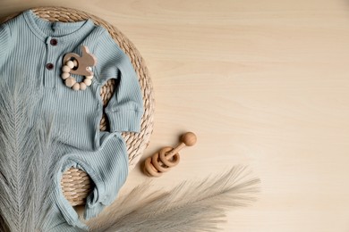 Baby bodysuit, toy and feather on wooden background, flat lay. Space for text