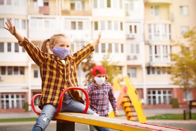 Little children with medical face masks on playground during covid-19 quarantine