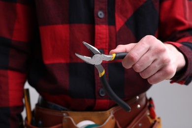 Photo of Young man holding pliers on grey background, closeup