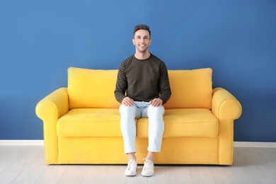 Photo of Handsome young man sitting on sofa, indoors