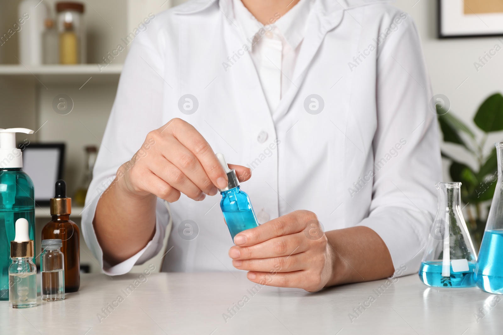 Photo of Dermatologist developing cosmetic product at white table indoors, closeup