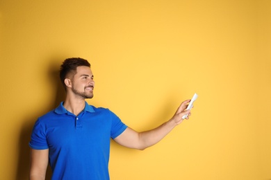 Photo of Happy young man operating air conditioner with remote control on yellow background. Space for text