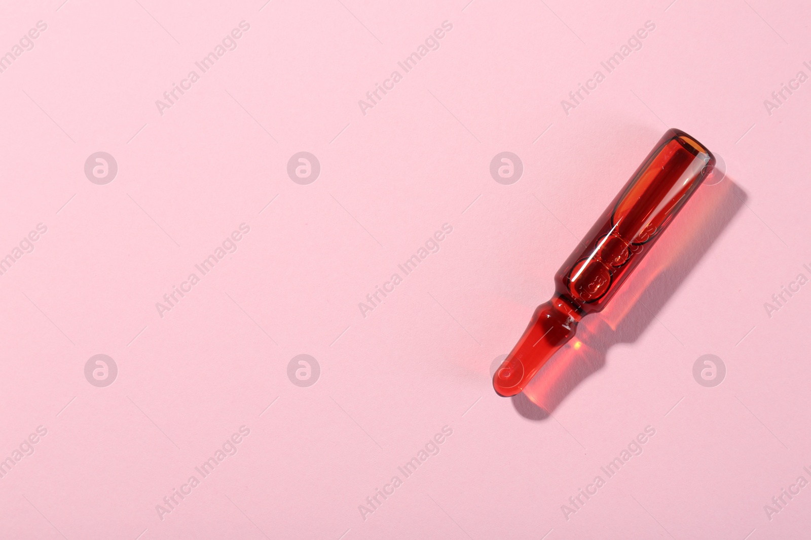 Photo of Glass ampoule with liquid on pink background, top view. Space for text