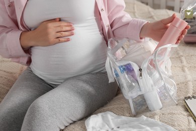 Photo of Pregnant woman packing baby stuff to bring into maternity hospital in bedroom, closeup