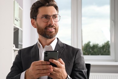 Photo of Handsome businessman using smartphone in office, space for text