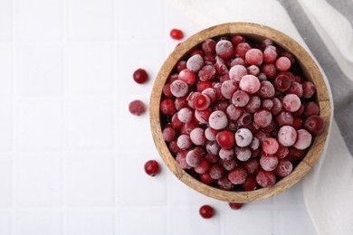 Photo of Frozen red cranberries in bowl on white tiled table, top view. Space for text