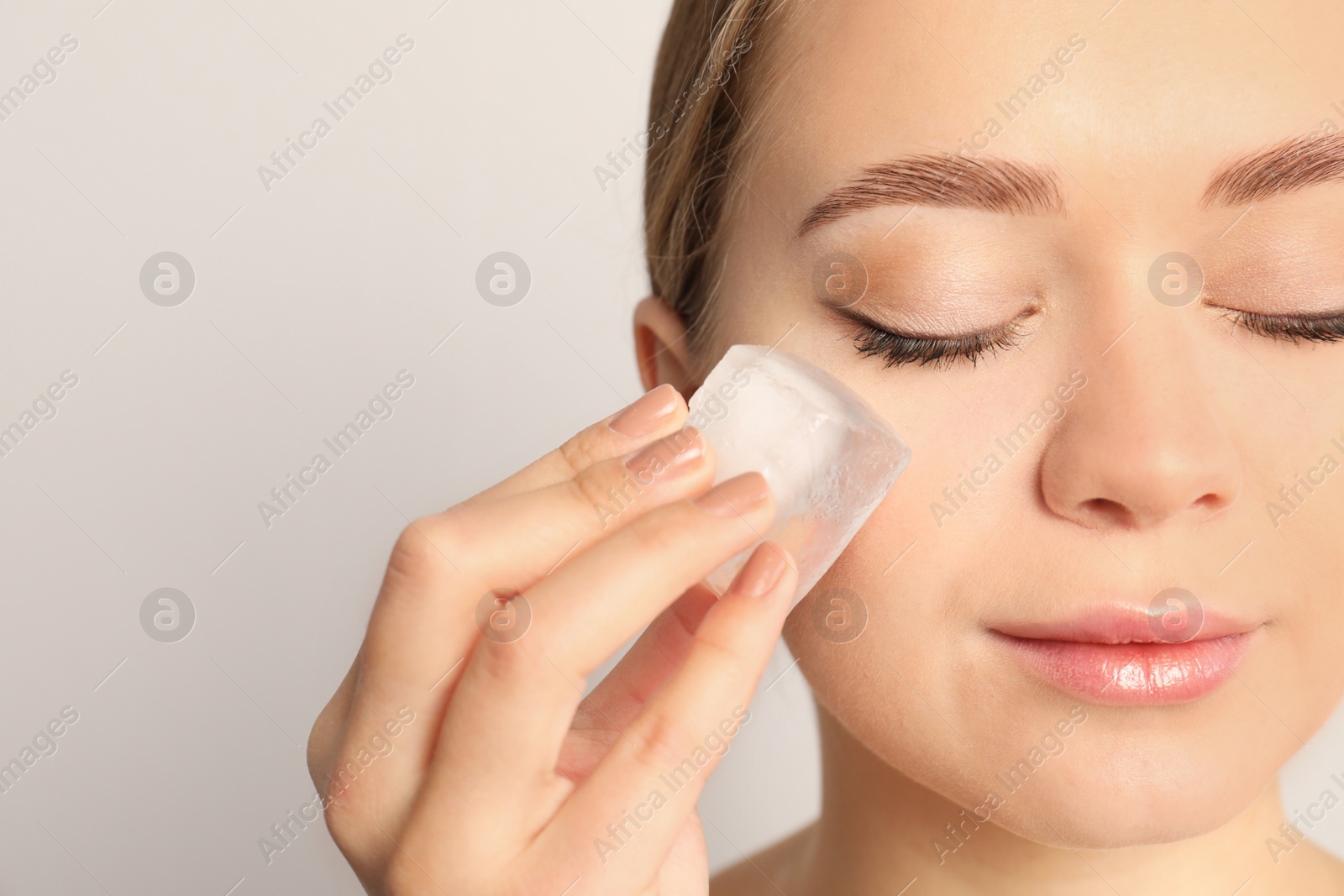 Photo of Young woman with ice cube on light background. Skin care